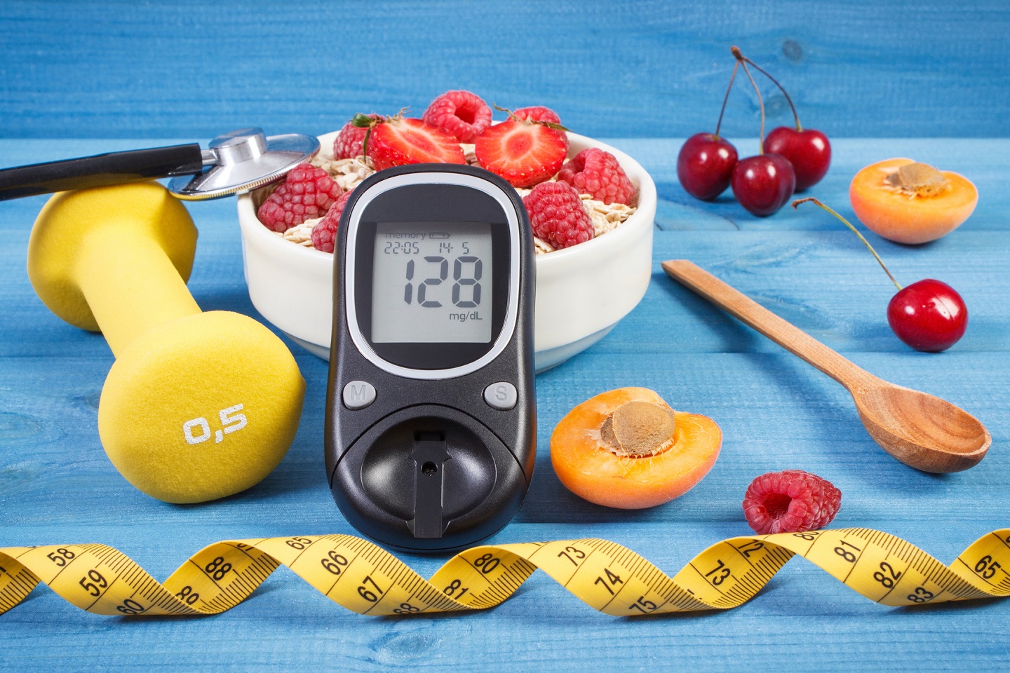 Un glucómetro junto a frutas, accesorios para hacer ejercicio físico y mantener un estilo de vida saludable